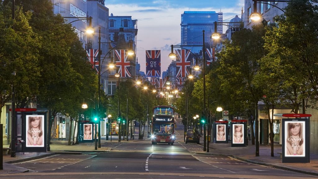 A city street with a double level bus in the distance - the street is lined with UK flags and digital displays
