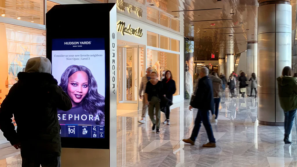 People walking through a retail shopping area with a person looking at a bright LCD digital display