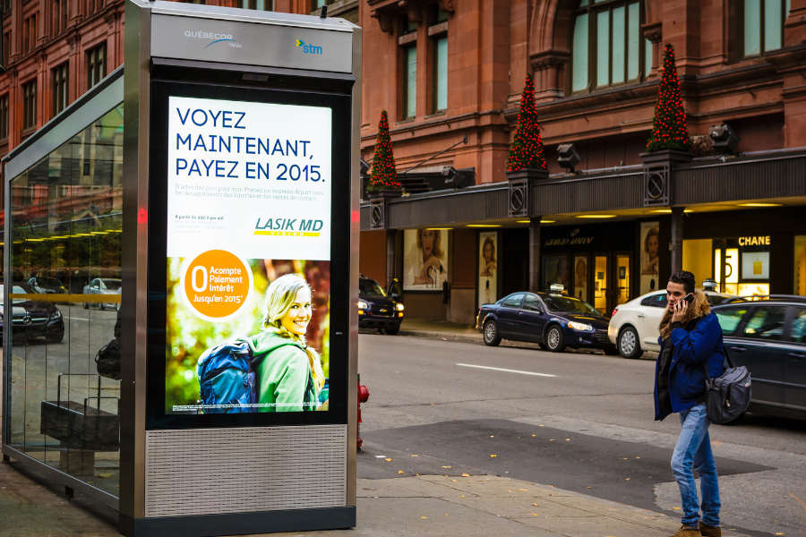 A digital display on the side of a metalic and glass bus station