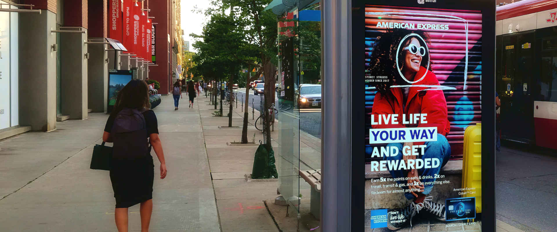 A woman walks by a colorful outdoor display mounted to a bus shelter