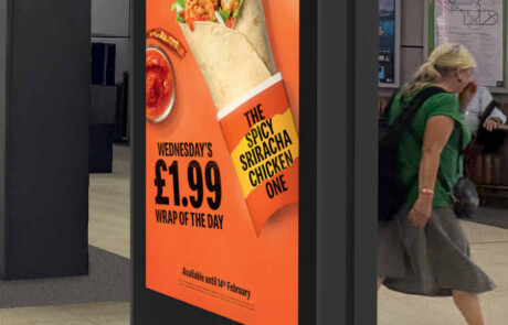 A vertical digital display in a subway station with woman walking by