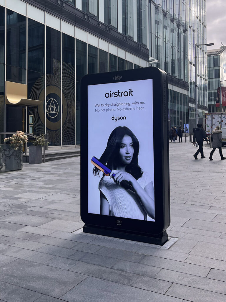 A digital ad for a hairbrush with woman in black and white on an outdoor LCD screen