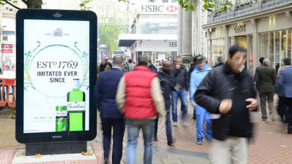 Street scene with a freestanding digital kiosk showing an HSBC ad amid pedestrians.