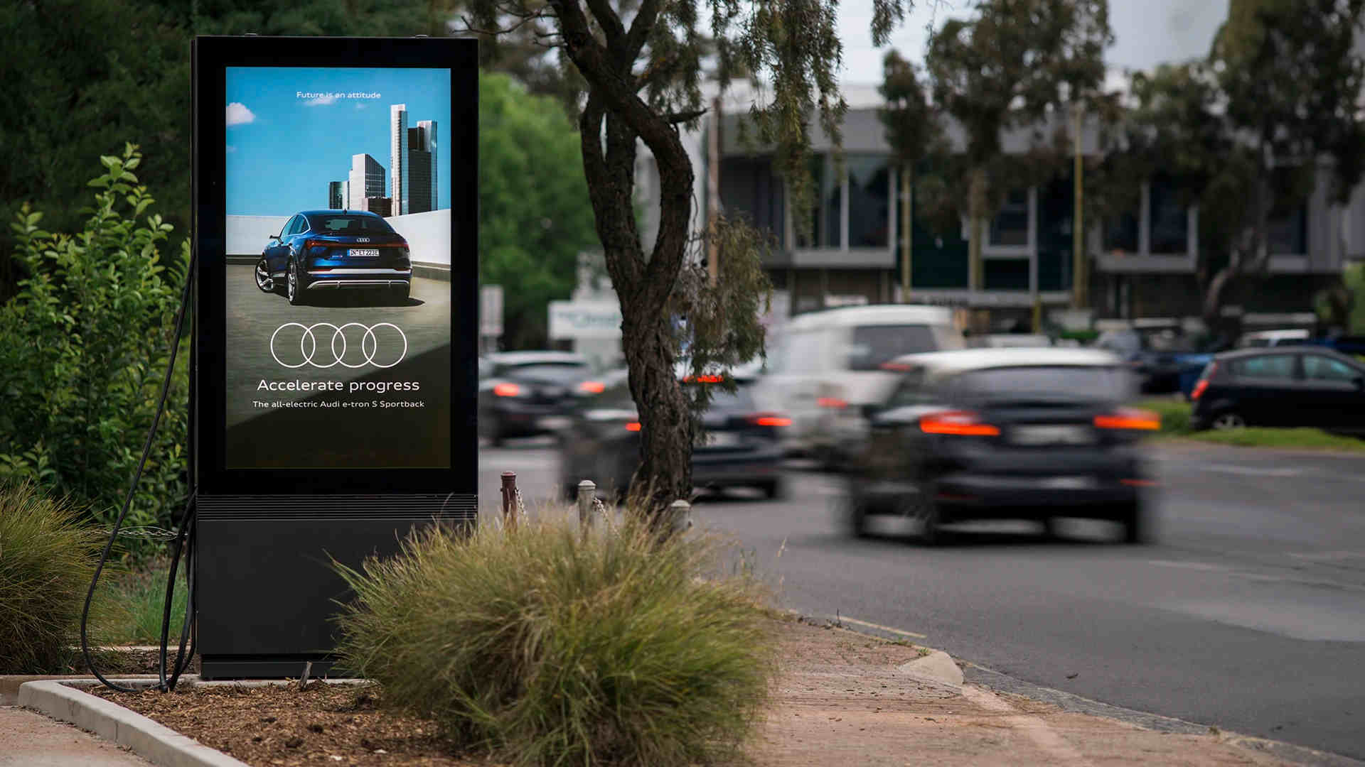 An outdoor display with EV charger shows an ad next to a busy street