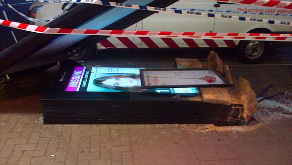 A toppled bus-shelter digital display lies on the sidewalk behind caution tape