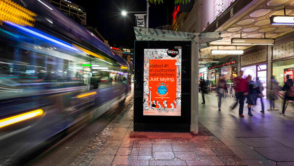 Nighttime bus-shelter ad panel with motion-blurred traffic and pedestrians
