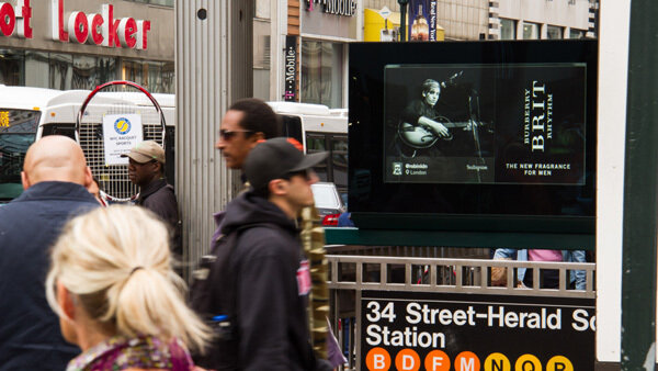 Subway entrance scene with a digital ad screen and people nearby