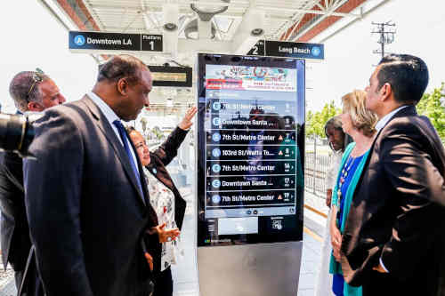 Well dressed people inspect a digital display that shows train times in a train station