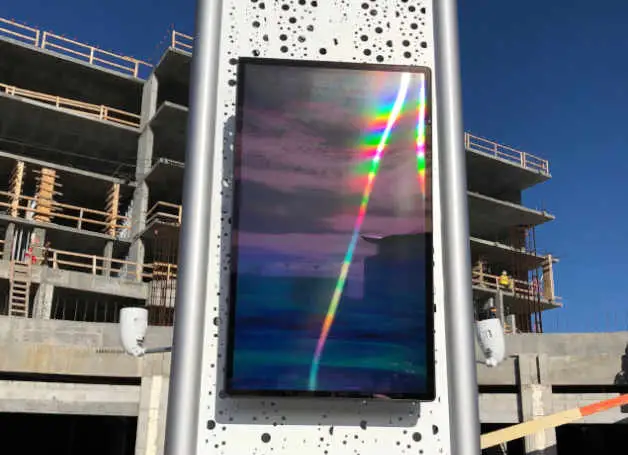 A long colored streak on a black screen mounted to a post and a building under construction in the background
