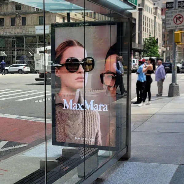 a woman with sunglasses in a digital display mounted on a glass bus shelter