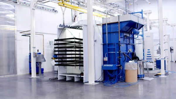 A white and grey facility with a large machine with a blue section that has frames being processed