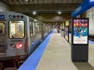 An underground train station with blue accent and a digital display on the walkway