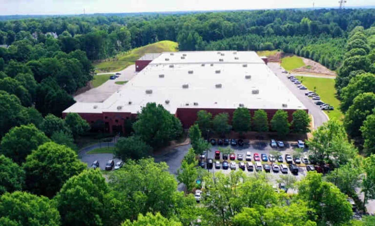A large facility from a birds' eye view surrounded by parking and a forest and trees
