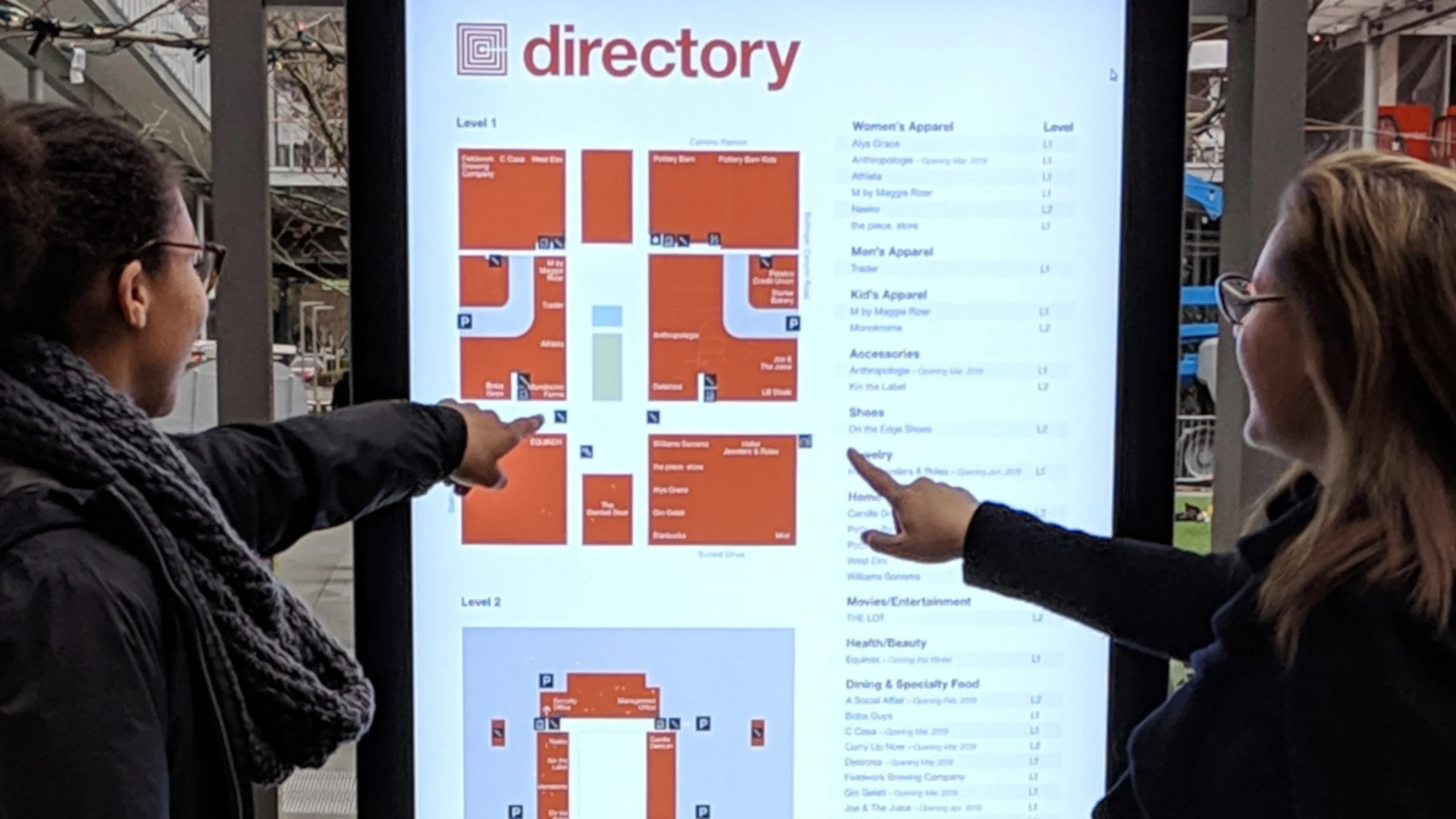 two women interact with a touch screen kiosk with a mall directory